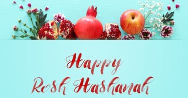 Imagem de várias frutas como romã e maçã decoradas com ramos de flores para compor os rituais para celebrar o ano novo judaíco. À frente dos elementos está escrito em inglês a frase: Happy Rosh HaShaná.