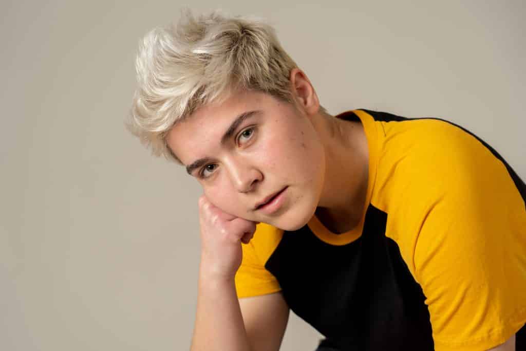 Imagem de um homem transexual. Ele usa cabelos curtos com reflexos dourados e veste uma camiseta nas cores preto e amarelo.
