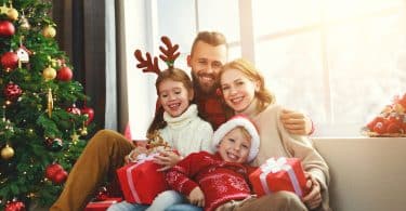 Uma família sentada no sofá enquanto abrem presentes de Natal