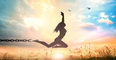 Silhueta de mulher pulando num campo, se livrando de uma corrente no tornozelo.