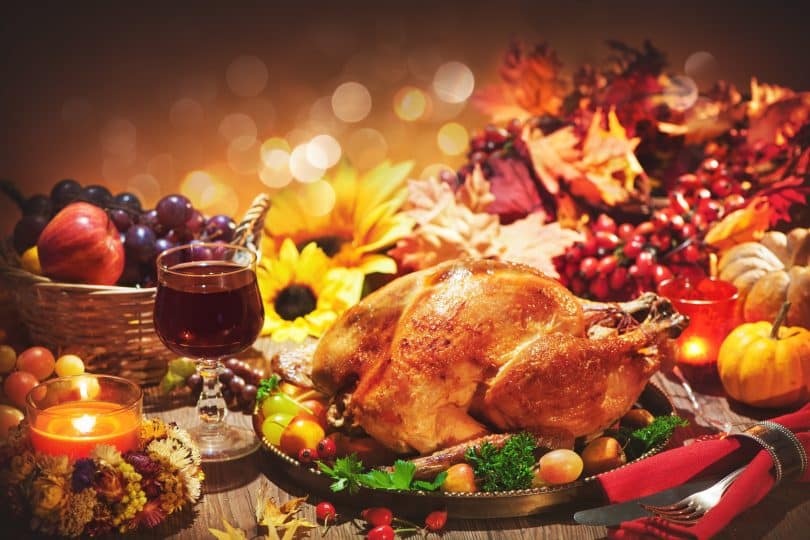 Imagem de uma linda mesa composta por vários tipos de comidas para celebrar o Natal. Temos: peru assado, frutas variadas, castanhas e vinho.