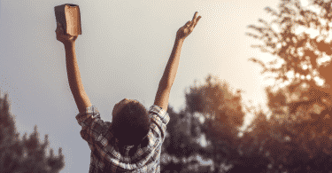 Homem segurando uma bíblia erguendo os braços pra cima