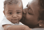 Mãe negra beijando rosto do filho bebê