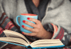 Mulher lendo um livro enquanto segura uma xícara de café