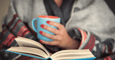 Mulher lendo um livro enquanto segura uma xícara de café