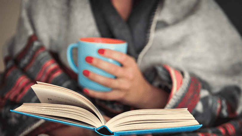 Mulher lendo um livro enquanto segura uma xícara de café