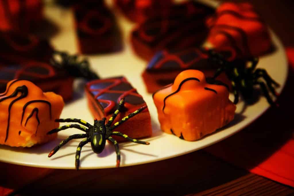 Imagem de um prato branco de porcelana repleto de doces decorados com aranhas e outros tipos de insetos para serem servidos no dia do Halloween.
