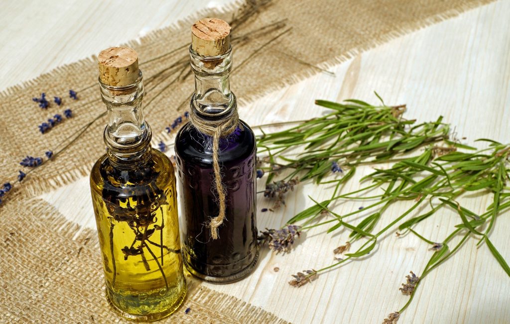 Imagem de dois fracos de florais dispostos sobre uma mesa forrada com toalha branca. Ao lado algumas flores que compõem ingredientes para o floral.