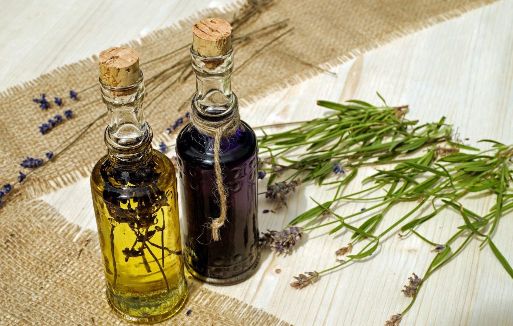 Imagem de dois fracos de florais dispostos sobre uma mesa forrada com toalha branca. Ao lado algumas flores que compõem ingredientes para o floral.
