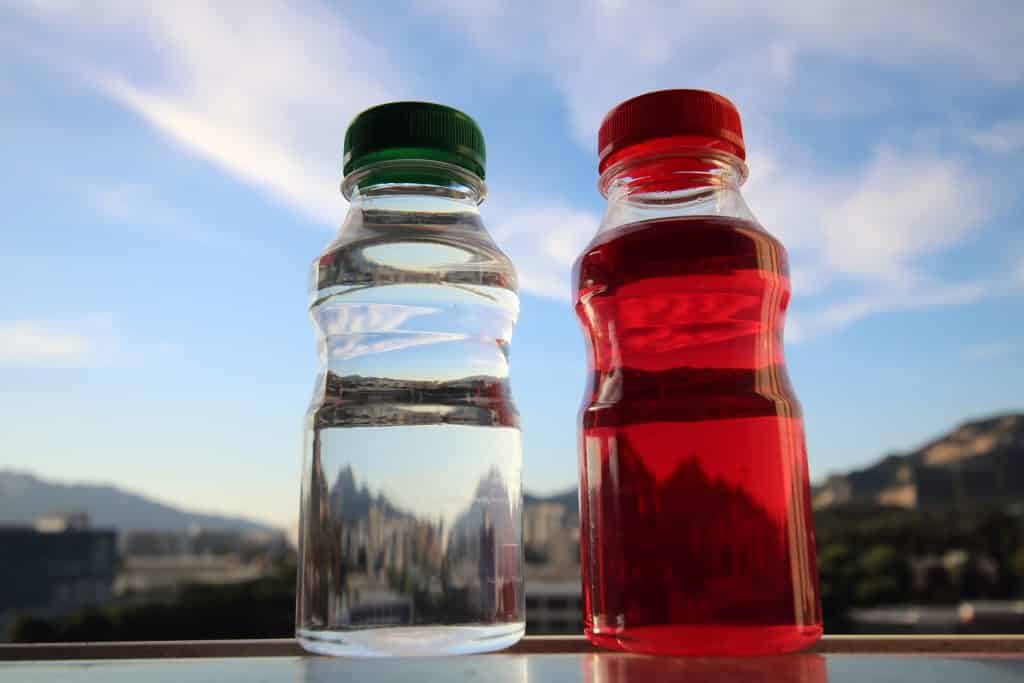 Imagem de duas garrafas, uma contendo água e a outra suco detox de hibisco desidratado.
