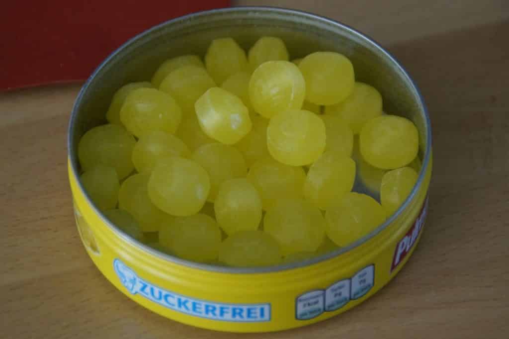 Imagem de um potinho amarelo contendo pequenas balinhas feitas de hortelã que são ótimas para dor de garganta.
