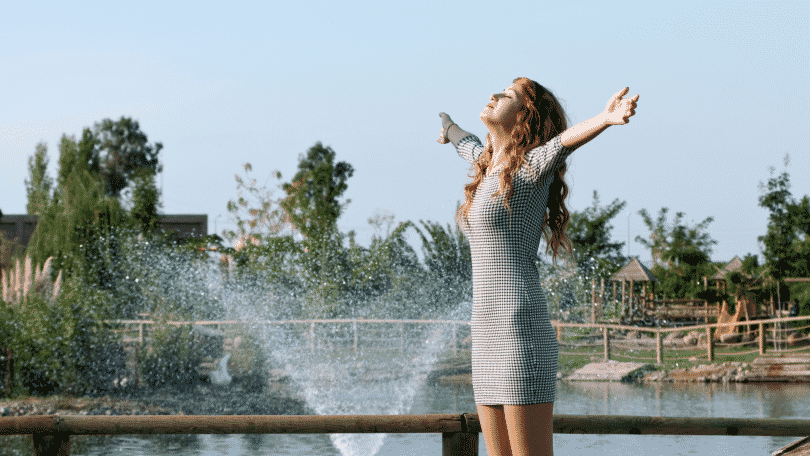 Mulher ruiva em um parque com os braços erguidos e sorrindo