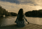 Silhueta de uma mulher meditando em um deck na frente do rio