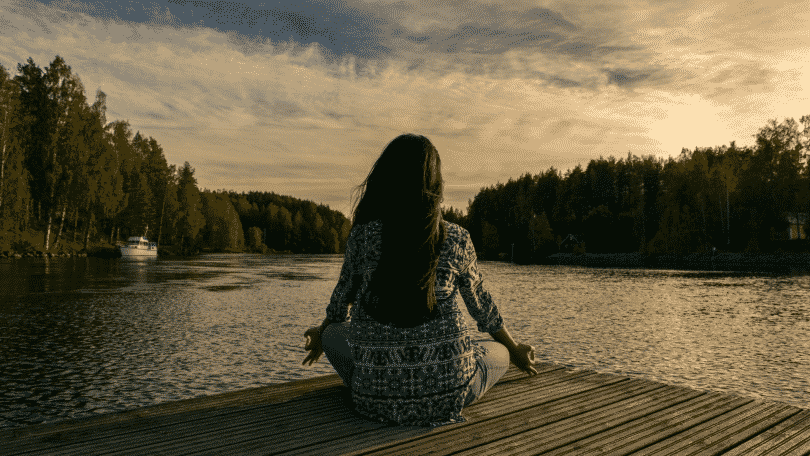 Silhueta de uma mulher meditando em um deck na frente do rio