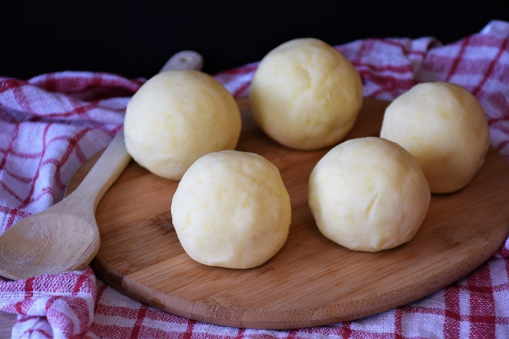 Imagem de cinco bolinhos feitos de peixe, dispostos sobre uma forma de madeira e ao lado uma colher de pau.