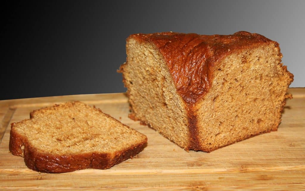 Imagem de um bolo de mel cortado ao meio e ao lado uma fatia, dispostos sobre uma tábua de madeira.