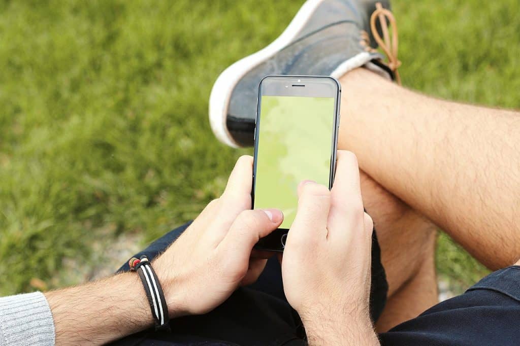 Imagem de um homem jovem, sentado. Ele está tentando acessar o celular, porém ele não está ligando.