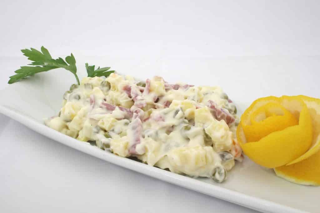 Imagem de um lindo salpicão vegano disponível em uma travessa de porcelana branca, decorado com cheiro verde e casca de laranja.