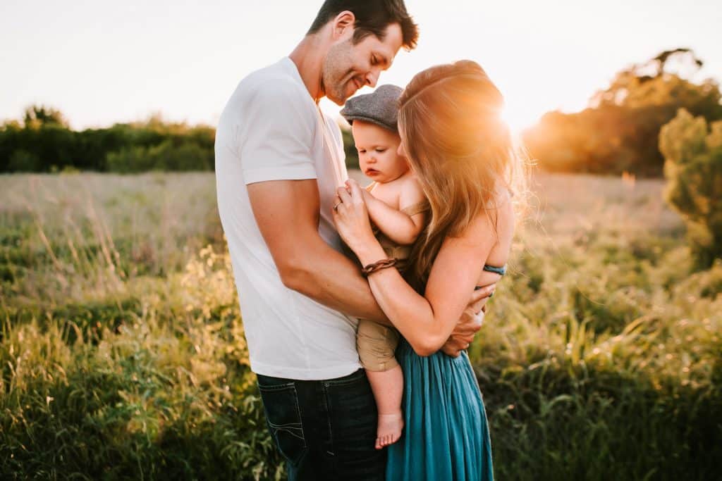 Homem e mulher brancos segurando bebê num campo.