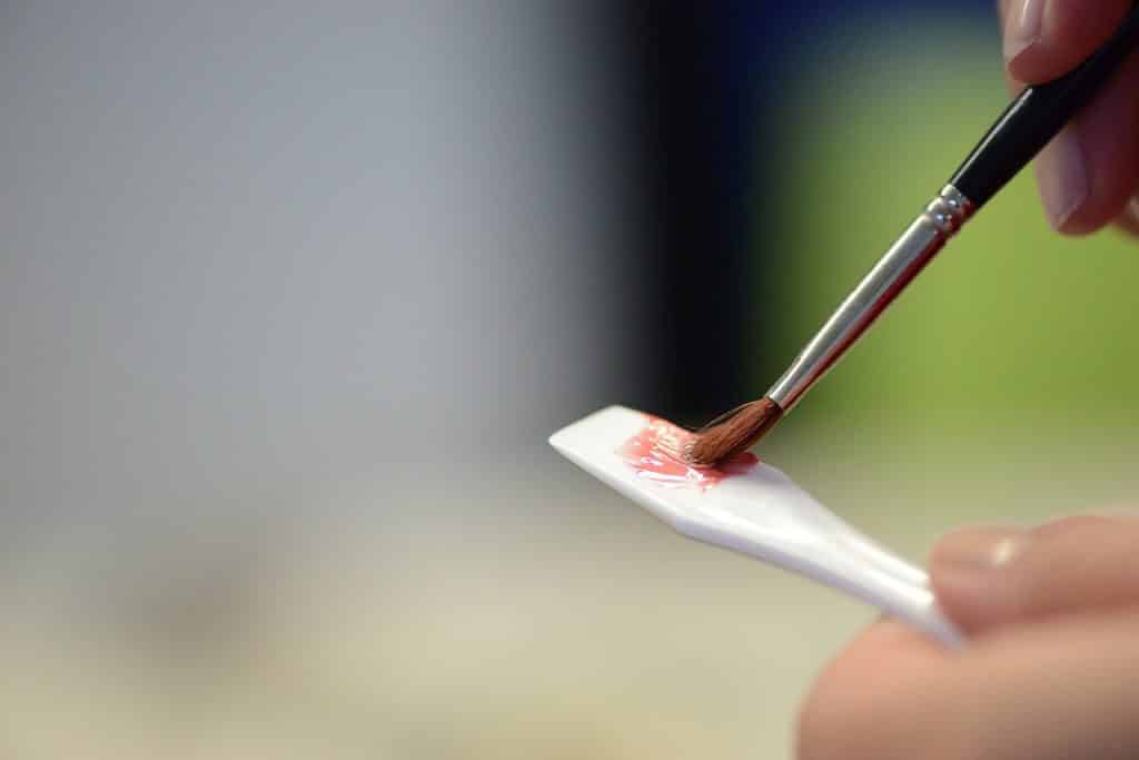 Mãos femininas misturando líquido rosa numa espátula.