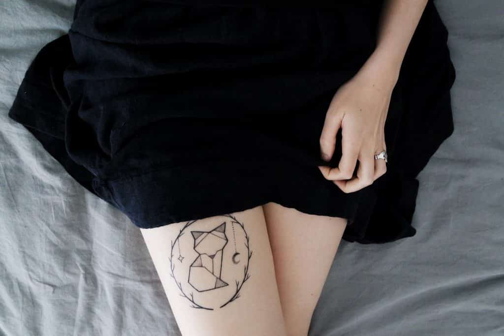 Imagem das pernas de uma garota e em uma delas a tatuagem do gato de uma bruxa.