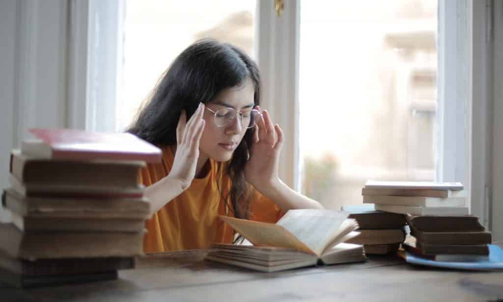 Menina com as mãos na cabeça de olhos fechados rodeada por livros