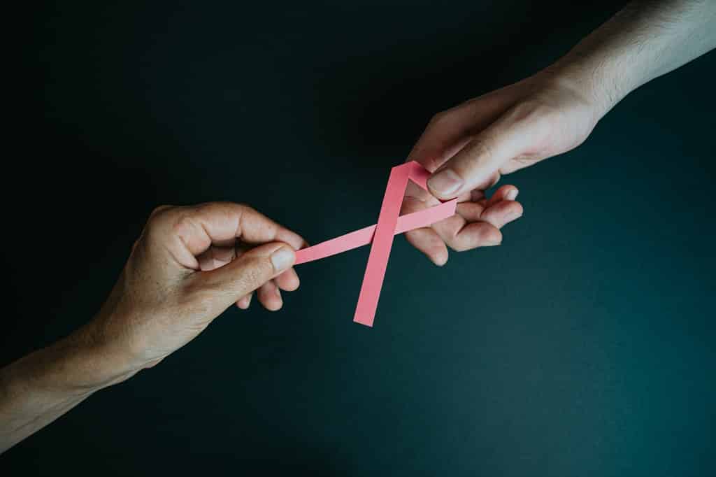 Duas mãos seguram laço rosa, simbólico do combate ao câncer de mama.