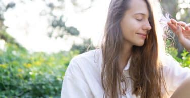 Mulher sentada em um jardim de olhos fechados segurando uma flor