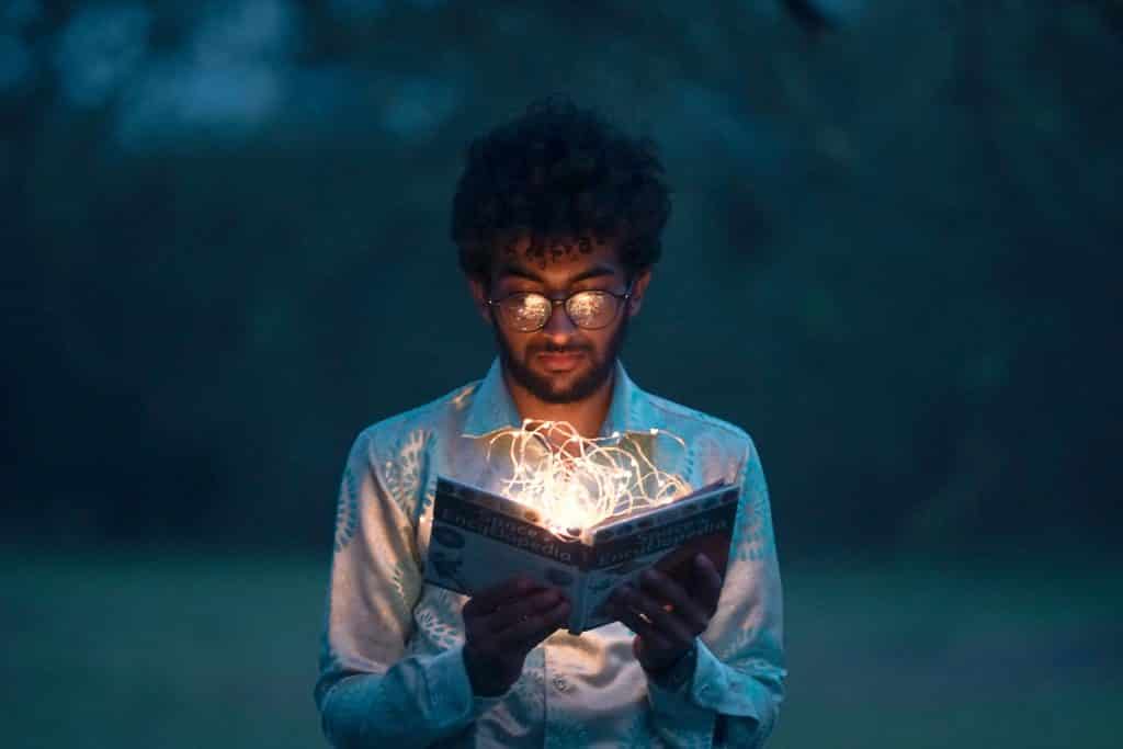 Homem lendo um livro com luzes saindo do livro representando o conhecimento  