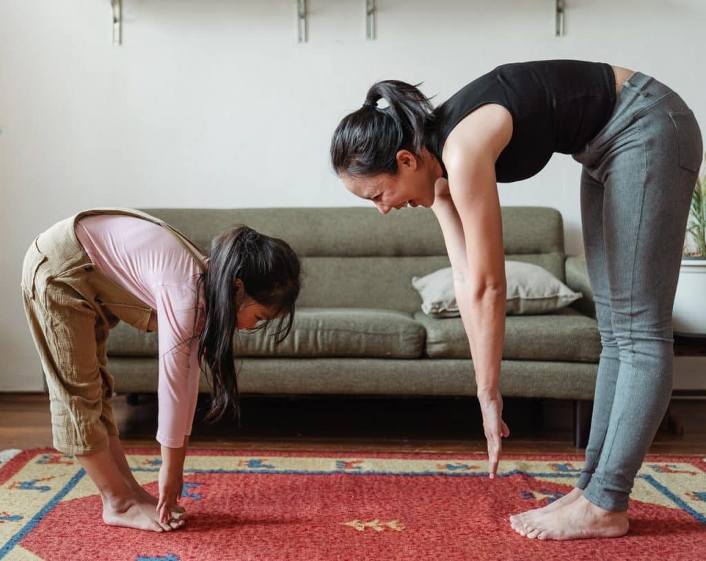 Mãe e filha alongando o corpo na sala de estar.