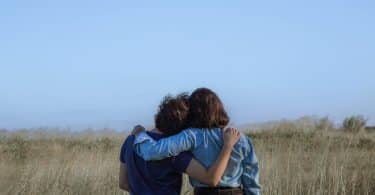 Duas pessoas abraçadas em um campo com gramado alto