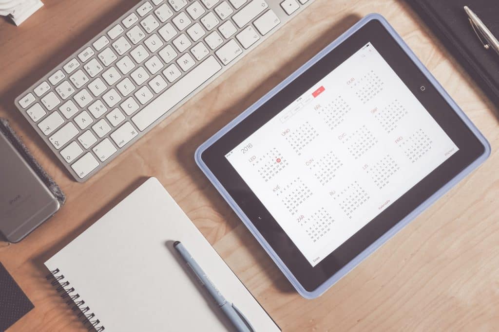 teclado de computador, um caderno e um calendário digital em cima de uma mesa