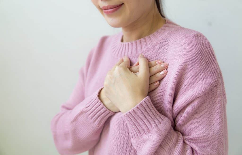 Mulher de suéter rosa segurando as mãos na altura do peito.