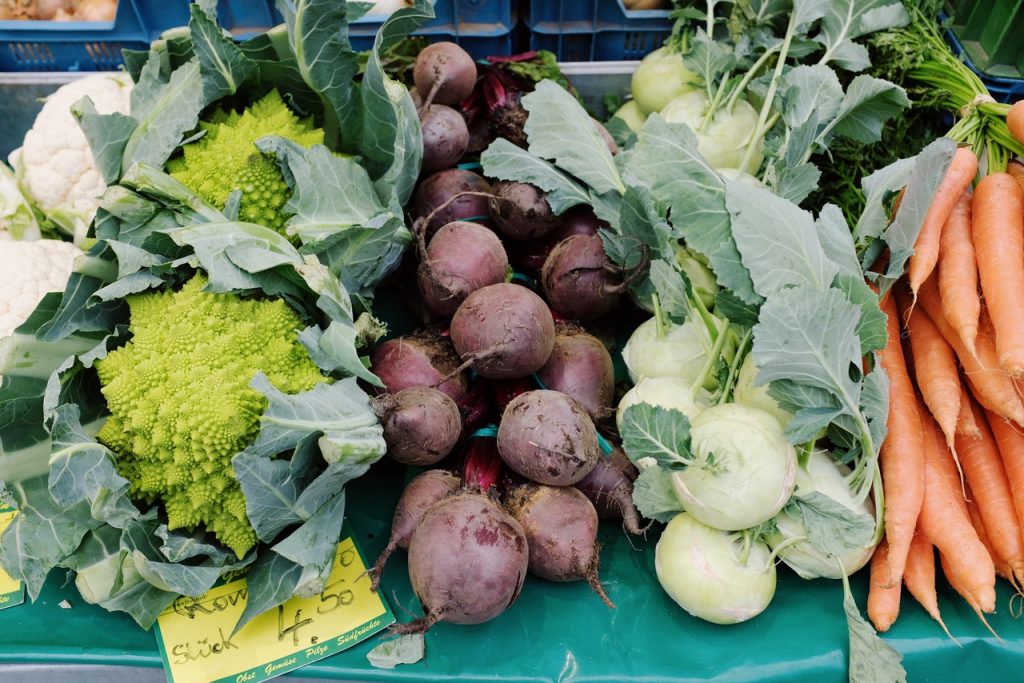 Foto de vegetais em uma banca. Há beterrabas, cebolas e cenouras.