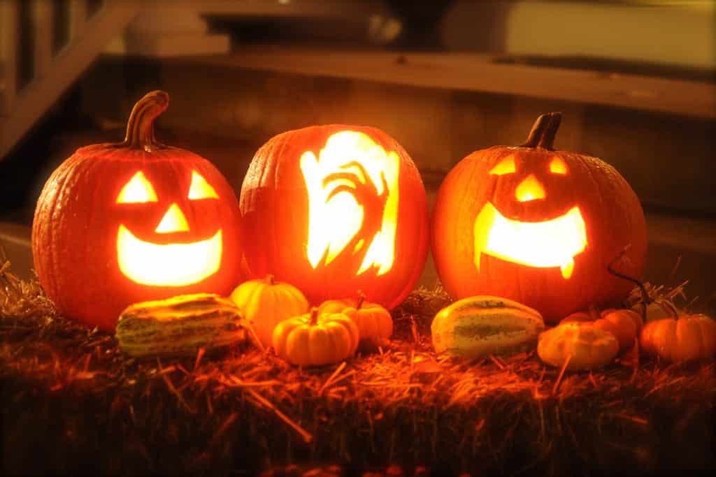 Imagem de três abóboras decoradas e iluminadas para enfeitar a comemoração do dia de halloween.
