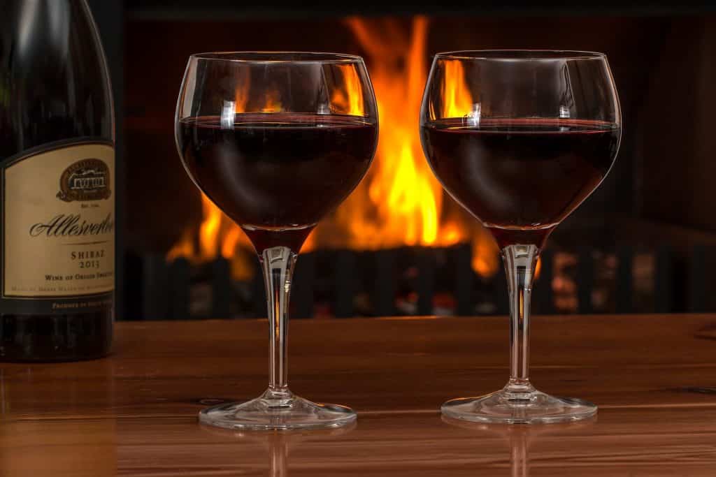 Imagem de duas taças contendo vinho tinto. Ao lado, uma garrafa de vinho.
