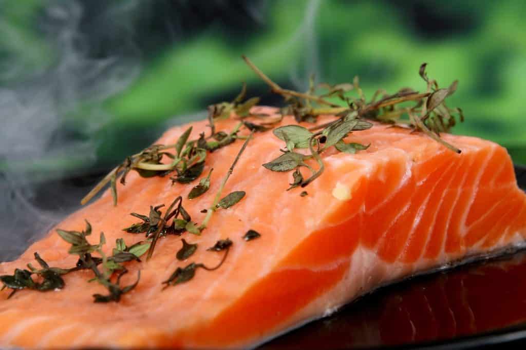 Imagem de um pedaço de salmão fresco e sobre ele alguns ramos de erva para tempero.