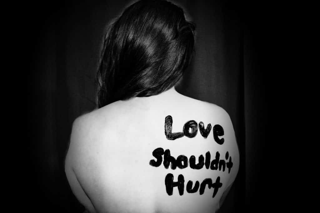 Mulher branca de costas com palavras escritas em tinta: "Love shouldn't hurt"