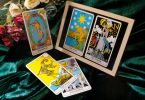 Imagem de uma mesa com cinco cartas de tarot dispostas sobre um pano verde brilhante. Ao lado um vaso com rosas coloridas.