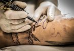 Imagem de um tatuador tatuando uma palavra no braço de um homem.