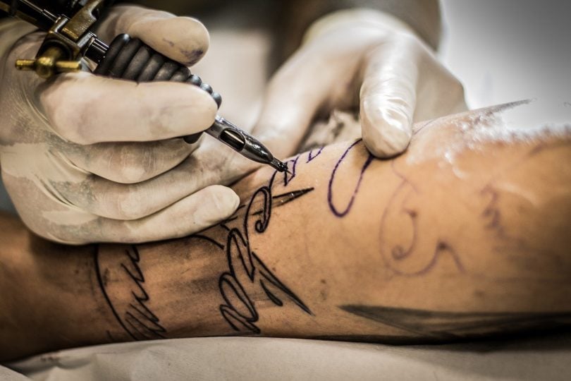 Imagem de um tatuador tatuando uma palavra no braço de um homem.