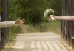 Imagem de uma passarela cercada. De um lado as mãos de um homem e do outro de uma mulher que segura um ramalhete de flor. Eles estão separados.