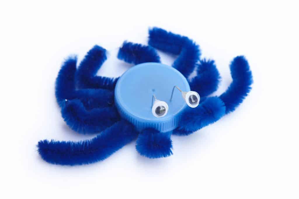 Imagem de um brinquedo reciclado feito de tampinha. É um inseto (aranha) na cor azul.