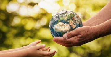 mãos de idoso dando o pequeno planeta Terra para uma criança sobre um fundo verde desfocado