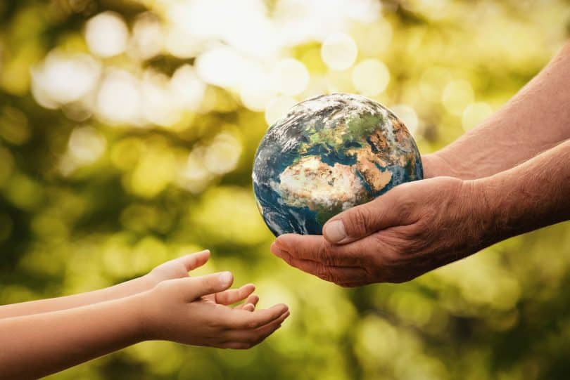 mãos de idoso dando o pequeno planeta Terra para uma criança sobre um fundo verde desfocado