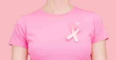 Mulher branca usando camiseta rosa com fita rosa cruzada.