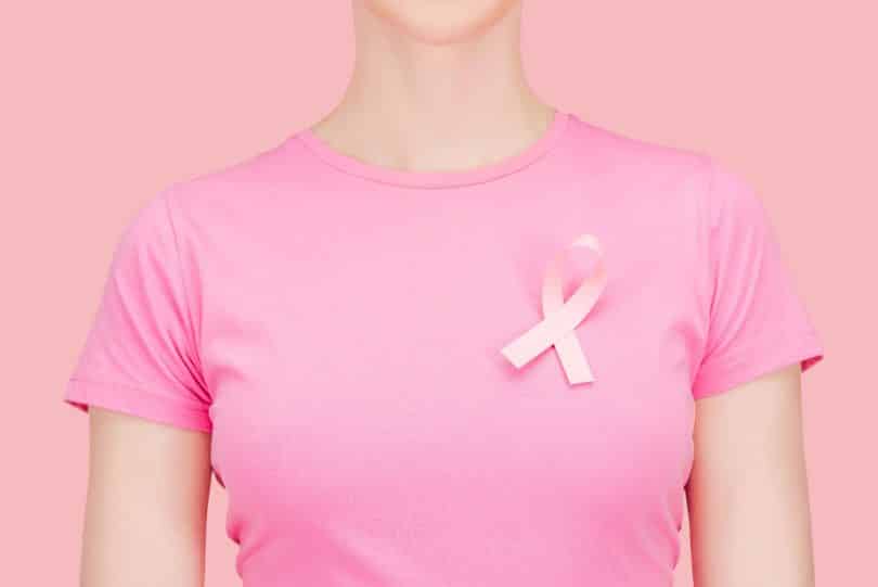 Mulher branca usando camiseta rosa com fita rosa cruzada.