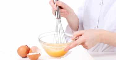Imagem das mãos de uma mulher mexendo os ovos em uma tigela de vidro. Ela está preparando uma hidratação para os cabelos feita com ovos.
