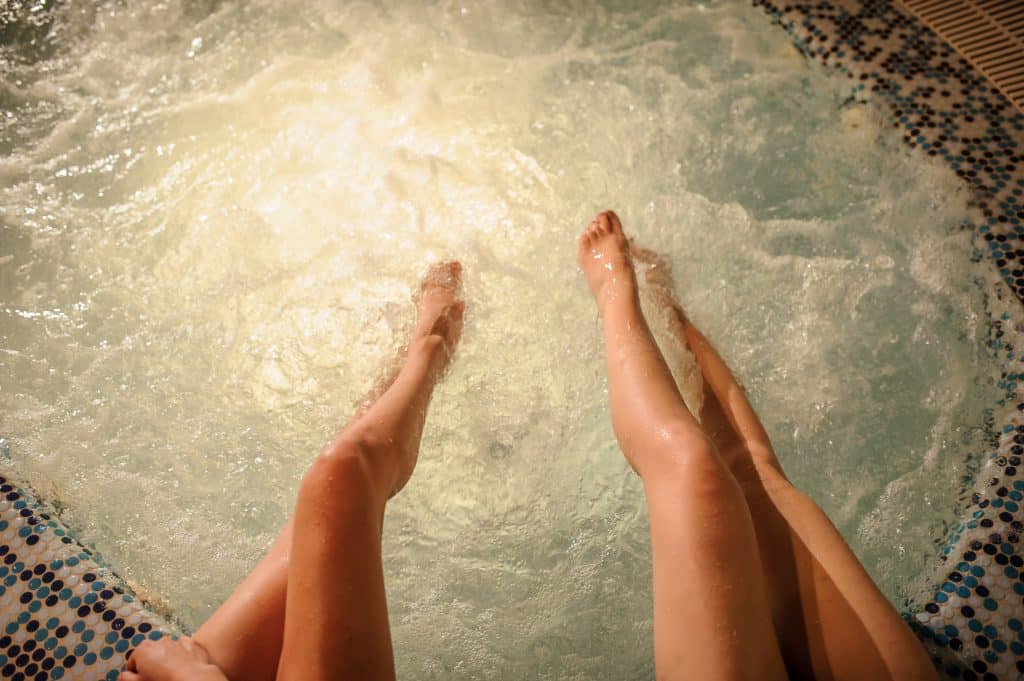 Imagem de duas pernas femininas dentro de uma banheira de hidromassagem.