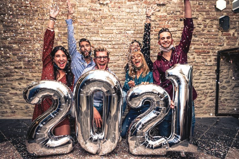 Pessoas Sorridentes com balões prateados celebrando o Ano Novo com máscara facial abaixada na época do coronavírus